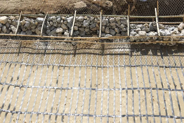 Zemin üzerinde kaya gabion sepeti ve çelik destek ızgarası bulunan eğim stabilizasyonunun yer aldığı inşaat alanı endüstriyel yapı sürecini gösteren somut çalışmalar için hazırlandı