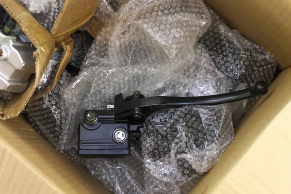 Parlak, yeni siyah motosiklet fren açma ana silindiri koruyucu plastik baloncuk ambalaj malzemeleriyle dolu kahverengi karton kutunun içinde otomotiv tamir bölümünün teslimatı için duruyor.