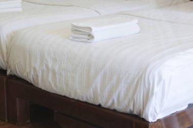 Lüks otel odasındaki rahat battaniyeli ve yumuşak yastıklı temiz beyaz yatak tatil gezisinde misafirlerin uyuması için rahatlatıcı bir ortam sunuyor.