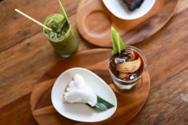 Tahta masadaki sağlıklı tatlı manzarası yeşil smoothie bardağı ve soğuk kahve içeceği beyaz tabağın yanında lezzetli ve rahatlatıcı kafe kahvaltısı zamanı için hindistan cevizli kremalı kek.