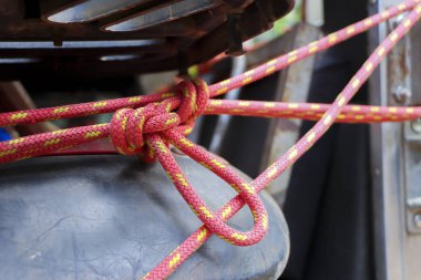 Güvenlik düğümüne bağlanmış kırmızı güvenlik halatının detaylı görüntüsü ekipmanların etrafına bağlanmış güvenlik duygusunu, hazırlığı ve güvenilirliği ifade eden gerilimi gösteriyor.