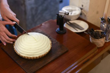 Profesyonel fırıncı dikkatli bir şekilde ev yapımı pastayı beyaz krema kaplı ahşap masa ile dilimliyor keskin bir bıçakla lezzetli bir tatlı hazırlıyor.