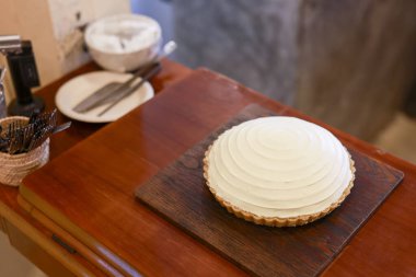 Ahşap masa arkasında tatlı tatlandırıcı beyaz kremalı tart tatlısı ev yapımı geleneksel hamur işlerinde fotokopi alanı ile ev yapımı hamur işlerinin keyfini çıkarıyor.