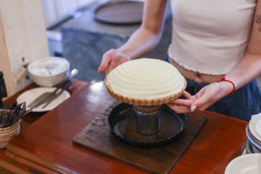 Genç bir kadın taze limonlu turtayı nazikçe tutuyor. Ev yapımı pastalı tatlıyı, ahşap tezgahta müşterilere servis etmeye hazır hale getirerek mutluluğunu gösteriyor.