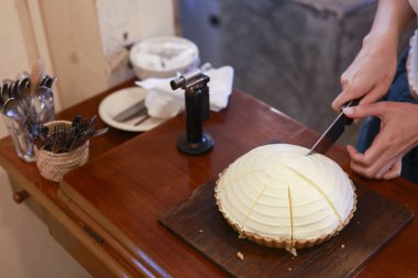 Elleri lezzetli kremalı peynirli turtayı ahşap masada bıçakla kesiyor. Tatlı tatlıyı dikkatlice hazırlıyor, aç müşterilere ikram ediyor. Sıcak kafe atmosferinde mutlu bir şekilde bekliyor.