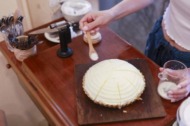 Profesyonel fırıncı lezzetli limonlu turtanın üzerine şeker serpiyor. Tatlıyı ahşap masada pürmüz ile karamelize etmeye hazırlanıyor. Titiz ve tutkulu hissediyor.