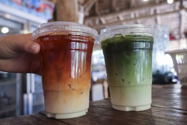 Buzlu Thai çayı ve yeşil kibrit latteyi ahşap masada, el ele tutuşup içecekleri içerken sıcak yaz gününde soğuk içecek isteyen susuz insanların rahatlığını gösteriyor.