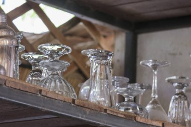 Temiz, boş cam bardak ve kadehleri düzenli ve düzenli duygusal ifadeyle kırsal restoran mutfağındaki ahşap raflara yerleştirin.
