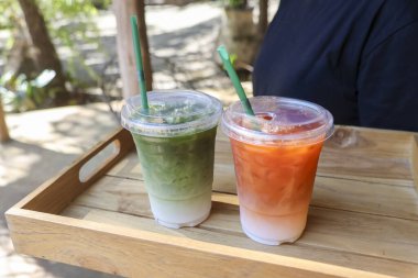 Soğuk, kibrit, latte yeşil çay ve limonlu çay, berrak plastik bardakta, ahşap tepside, yazın açık hava kafeteryasında neşeli bir şekilde servis edilir.