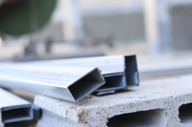 Gri çimento bloğu istiflenmiş dikdörtgen metal boru kirişleri ve bulanık arkaplanlı güçlü endüstriyel konsepti ve dayanıklı sağlam malzemeyi gösteren inşaat alanı.