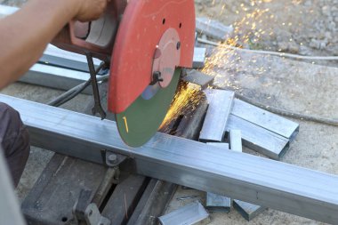 İşçi el testeresi ile metal kesme işlemi parlak turuncu kıvılcımlar, inşaat alanında çelik imalatı gündüz ağır iş gücü olduğunu gösteriyor.