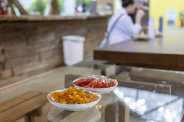 Yan yemek ve aperatifleri Cafe 'deki cam masadaki iki küçük beyaz kaseye koy. Bulanık arka plan kadınların yemek yediğini, sakin ve sıradan yemekler yaptığını gösteriyor.