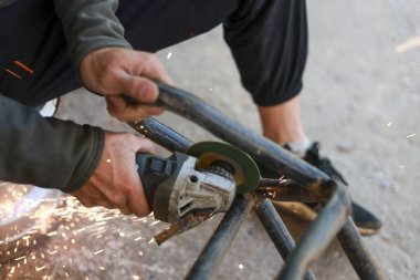 Açı öğütücüyle metal boru kesmeye odaklanmış bir işçi. Atölyede inşaat sırasında kıvılcımlar uçuşurken, insanın el ele tutuşan elektrikli aletini kapat