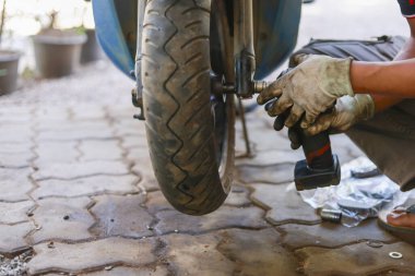 Garajdaki odaklanmış tamirci, motosiklet tekerleği tamiri ve lastik bakımı yapıyor. Profesyonel hizmet, gayretli çalışma ve uzmanlık için kullanılan araç