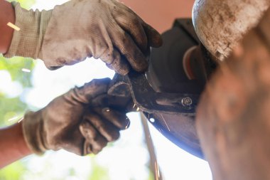 Elektrikli aletle metal kesen bir adamla odaklanmış el emeği. Kirli eldiveni, kıvılcımlar saçan bir açı öğütücü kullanarak kapat. Endüstriyel tamir