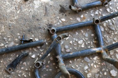 Grunge Beton zemin üzerinde parçalanmış, kirli metal motosiklet iskeletinin endüstriyel yakın çekimi. Atölyede tamir, hurda veya montaj için parçaların ayrıntılı görünümü