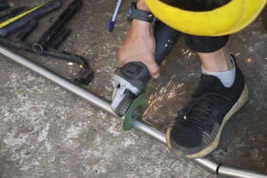 Açı öğütücüyle metal boruları keserek parlak kıvılcımlar oluşturarak atölyede odaklanmış bir işçi. Sanayi süreci iş için güvenlik ve kesinlik gerektirir