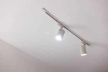 Temiz tavanda iki parlak spot ışığı olan modern beyaz yol aydınlatması. Çağdaş ev, galeri veya ofis odaklı aydınlatma için basit iç tasarım