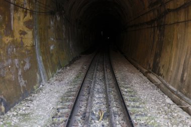 Eski bir yeraltı tünelinin içindeki karanlık tren yolu. İleriye dönük bakış açısı gizeme ve bilinmezliğe götürür, gizemli ve ürkütücü bir his yaratır.