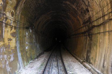 Bilinmeyen karanlığa giden tren rayları olan karanlık, gizemli tren yolu tüneli. Korkunç yeraltı geçidi yolculukta belirsizlik ve korkuyla dolu bir yol oluşturuyor.