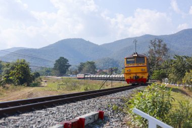 Manzaralı demiryolu üzerindeki sarı dizel tren kırsal alanda seyahat ediyor. Yolcu arabalı klasik lokomotif Tayland 'da dağ geçmişine sahip kırsal kesimde seyahat ediyor.