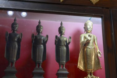 Sıraya dizilmiş dört antik Buda heykeli. Altın heykel, kırmızı arka plana karşı koyu bronz figürler arasında duruyor, sükunet ve kültürel saygıyı çağrıştırıyor.