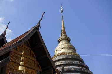 Açık mavi gökyüzü altında, Tayland 'daki altın stupanın ve geleneksel tapınağın huzurlu manzarası. Görkemli antik Tayland mimarisi ve inşaatı barış için ilham verici.