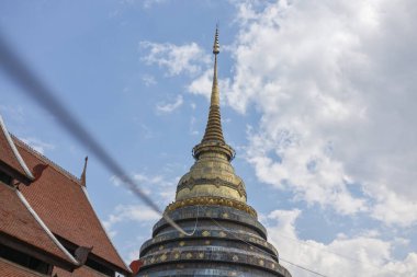 Tayland 'daki Budist tapınağındaki altın stupanın sakin manzarası. Antik dini mimari parçalı bulutlu gökyüzü arka planına karşı dimdik ayakta duruyor