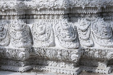 Karmaşık taş oyma ile beyaz Tayland tapınak duvarının huzurlu manzarası. Ayrıntılı heykel, şablon ve mimariye yakın çekim. Güzel geleneksel işçilik sergiler.