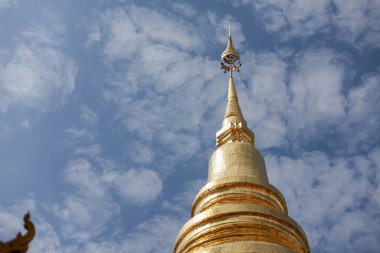 Asya 'daki manevi Budist tapınağındaki altın pagoda kulesinin sakin açısı. Görkemli mimari beyaz bulutlu güzel mavi gökyüzüne karşı dimdik ayakta duruyor.