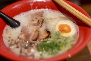 Lezzetli Japon ramen çorbası ve kırmızı kase. Tuzlu domuz eti, kaynamış yumurta ve kremalı tonkotsu çorbası içinde yeşil soğan. öğle veya akşam yemeği için sıcak ve rahatlatıcı yemek