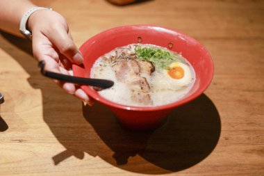 Lezzetli Japon ramen çorbası, yumuşak domuz eti ve haşlanmış yumurta. Elleriniz kaşığı sıcak, rahatlatıcı yemeğin üzerinde tutar. Lezzetli yemek hazır.