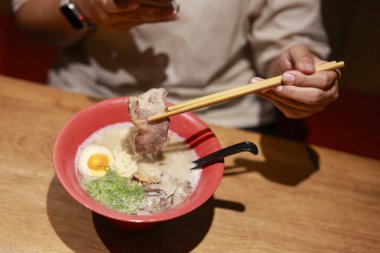Japon eriştesi çorbası yiyen kişi. Restoranda yemek çubuğuyla domuz eti tutuyorum. Eğlenceli ve tatmin edici bir yemek deneyimi.