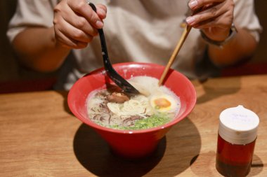 Japon eriştesi çorbası yiyen memnun bir insan. Lokantadaki geleneksel yemek manzarası, keyif ve otantik mutfak kültürünü gösteriyor.