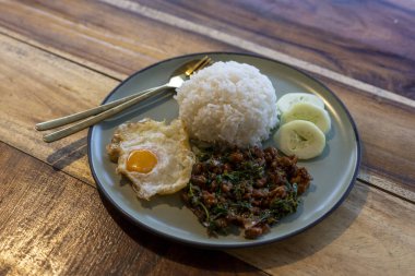 Lezzetli ve iştah açıcı Tayland yemeği, Pad Krapow, kutsal fesleğenle yapılan popüler baharatlı yemek, kıyma domuz eti, pirinç ve ahşap masada kızarmış yumurta.