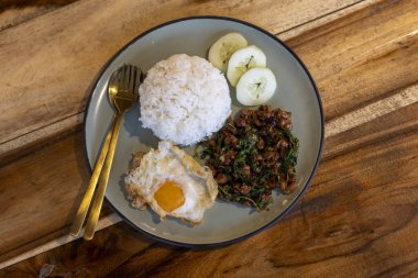 Lezzetli Tayland yemeği tabağı, kıyılmış domuz kızartması, kutsal fesleğen ve pirinçli kızarmış yumurta. Ahşap masada leziz bir yemek.