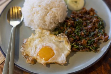 Lezzetli Tayland fesleğeni kızartması, kıymalı baharatlı yemek ve pilav üzerine kızarmış yumurta. İştah açıcı yemek ve Tayland 'dan gelen popüler sokak yemekleri rahatlatıcı bir lezzet sunuyor.
