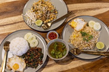 Geleneksel Tayland yemeği için nefis bir manzara. Lezzetli tabaklar dolusu kızarmış pirinç, erişte ve ahşap masada fesleğen domuz eti iştah açıcı bir akşam yemeği ya da öğle yemeği deneyimi yaratır.
