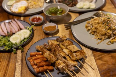 Ahşap masada geleneksel Tayland yemeklerinin lezzetli çeşitleri. Asya mutfağında mükemmel bir akşam yemeği için tavuk satay, domuz rostosu ve baharatlı pilav ile iştah açıcı yemek.