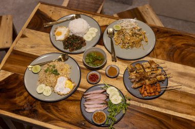 Kırsal ahşap masada iştah açıcı bir Asya yemeği ziyafeti. Bu yemekte kızarmış pilav, ızgara satay şiş, et ve çeşitli baharatlı soslar var. tatmin edici yemek.