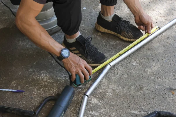 Metal boruları ölçmek için mezura kullanan odaklanmış bir işçi. Adam atölyedeki inşaat projesinde çalışıyor. Hassasiyet ve konsantrasyonla riskli işler yapıyor.