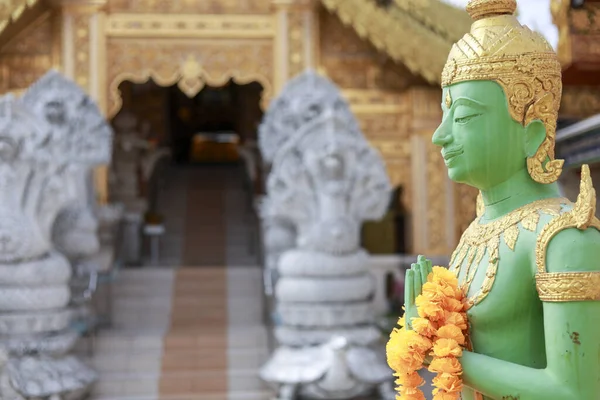 Huzurlu yeşil koruyucu ilah heykeli geleneksel Tayland tapınağının girişinde huzurlu bir ifadeyle. Bu süslü heykel Asya dini, sanatı ve kültürünü yansıtıyor.