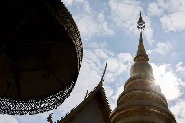 Tayland 'daki sakin Tayland tapınağındaki altın çedi kulesinin alçak açılı görüntüsü. Parlak güneşli mavi gökyüzüne karşı geleneksel şemsiye huzur verici, ruhani bir sahne yaratıyor