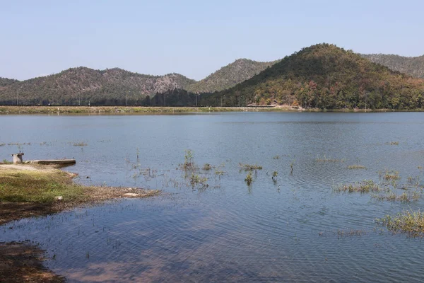 Sakin göl ve yeşil dağ sırasının huzurlu yaz manzarası. Bu dingin ve sakin doğal manzara, berrak gökyüzü rahatlama anı sağlar.