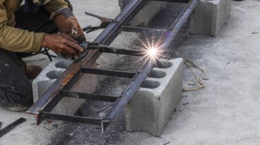 Ağır metal kaynaklı, parlak kıvılcımlı, becerikli bir işçi. Sert inşaat atölyesinin zemininde yoğun bir atmosfer yaratıyor.