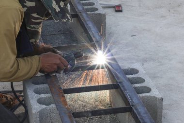 Profesyonel endüstriyel kaynakçı inşaat fabrikasındaki çelik yapıyı kesiyor. Parlak sıcak kıvılcımlarla üretiliyor. Yoğunlaştırılmış ve dikkatli bir ruh hali yaratıyor.