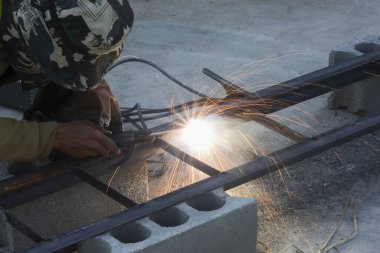 İnşaat işçisi çelik çerçeve kaynak yapıyor. Açık havada parlak kıvılcımlar yaratıyor. Sıkı çalışma ve kendini adama işçiliği ile.