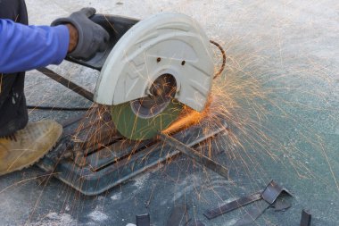 Metal çubuğu elektrik kesme makinesiyle kesen endüstriyel işçiler inşaat alanında yoğun odaklanma ve yoğun duygularla parlak turuncu kıvılcımlara neden oluyorlar.