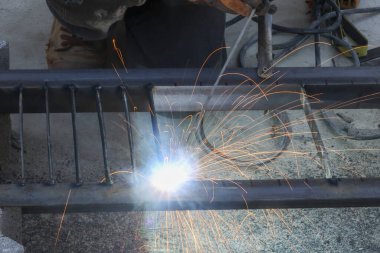 Metal yapımında meşale kullanan endüstriyel kaynakçı atölyede parlak ışık ve sıcak kıvılcımlarla kendini adamış ve yapıya odaklanmış zanaatkarlığı gösteriyor.