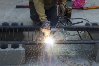 Güçlü inşaat iskeleti için uçan kıvılcımlar ve parlak parlayan metal yapısıyla çalışan odaklanmış erkek kaynakçı dışarıda endüstriyel iş onarımı yapıyor.